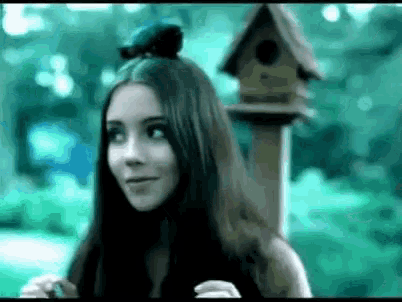a woman with a bird on her head standing next to a bird house .