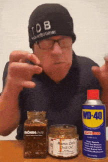 a man wearing a hat that says tdb is holding a can of wd-40