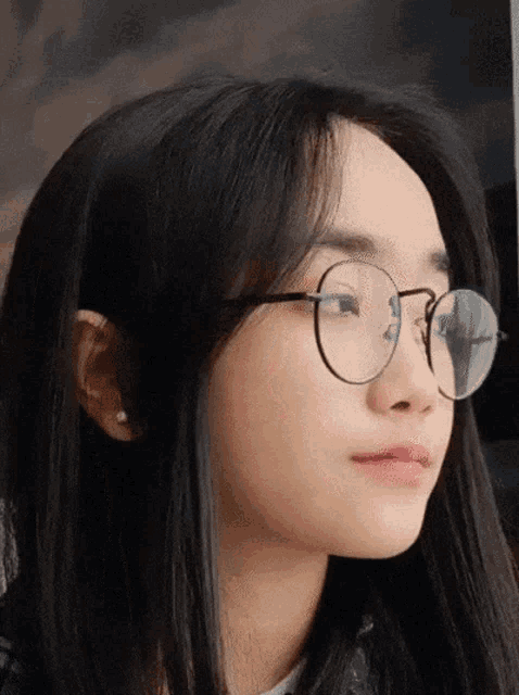 a woman wearing round glasses and earrings looks to the side