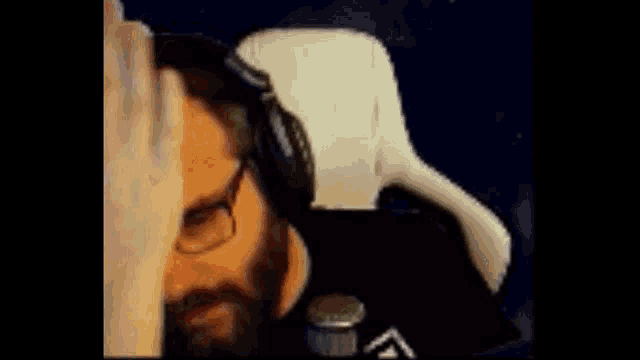 a man with glasses and a beard is holding his hand to his head .