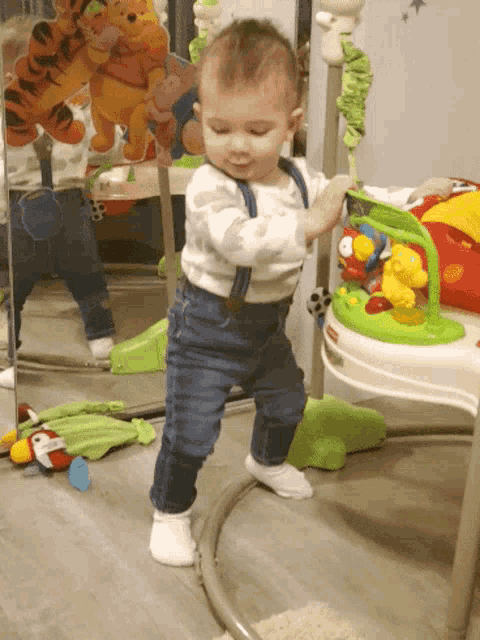 a baby is standing in front of a mirror playing with a toy