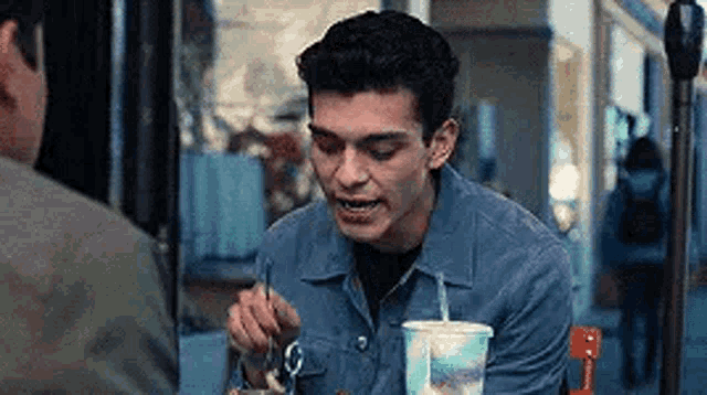 a young man is sitting at a table eating a meal and drinking a drink .