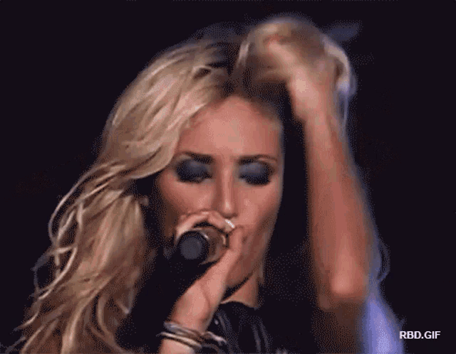 a blonde woman is singing into a microphone with rbd.gif below her