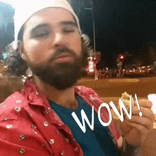 a man with a beard is holding a piece of food and says wow .