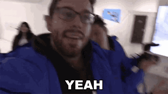 a man wearing glasses and a blue jacket says yeah in a blurry photo .