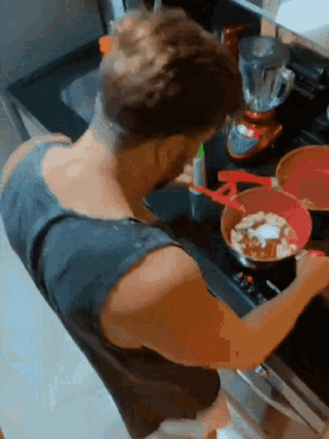 a man in a black tank top is cooking on a stove top