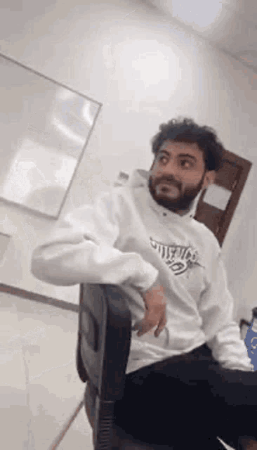 a man with a beard is sitting in a chair in front of a whiteboard .