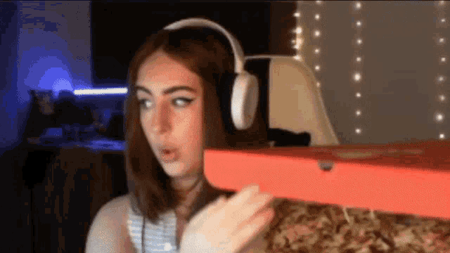 a woman wearing headphones holds a pizza box in her hand