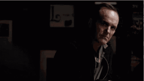 a man in a black jacket is holding a glass of whiskey in his hand in a dark room .