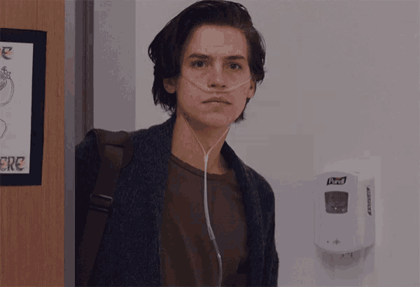 a young man wearing an oxygen mask is standing in front of a hand sanitizer dispenser that says purell