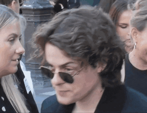a woman wearing sunglasses talks to a man in a crowd of people