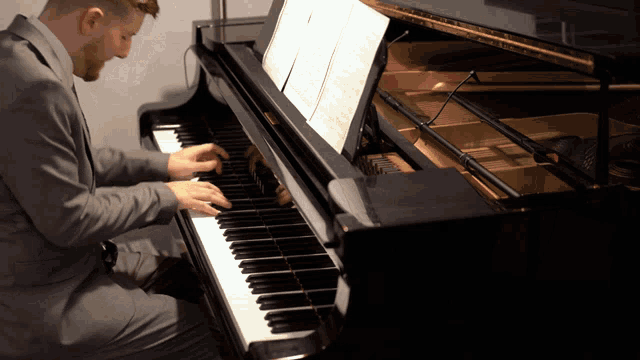 a man in a suit is playing a piano with the sheet music visible