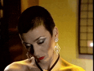 a woman with short hair and earrings is wearing a yellow dress and a black necklace .