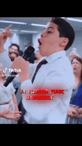 a boy in a white shirt and tie is singing into a microphone in front of a crowd of people .