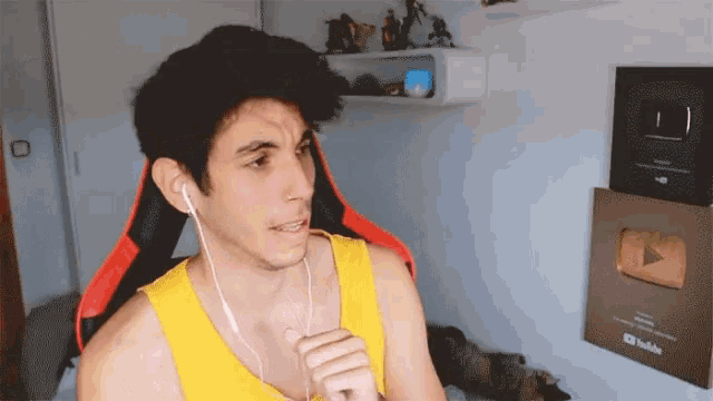a man wearing a yellow tank top and ear buds stands in front of a youtube plaque