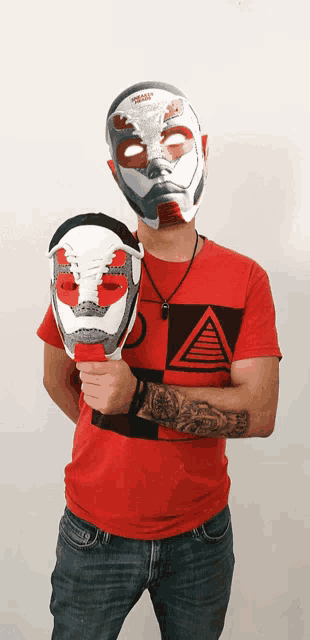 a man wearing a red shirt with a triangle on it is holding two masks in front of his face