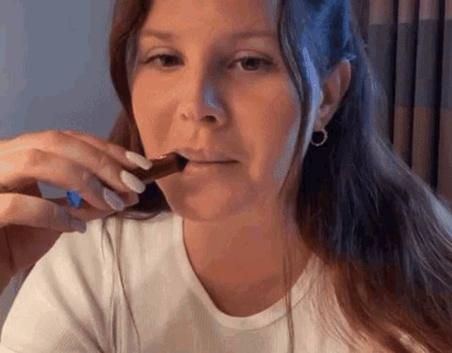 a woman in a white shirt is eating a chocolate bar with a spoon .
