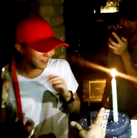 a man in a red hat stands in front of a birthday cake