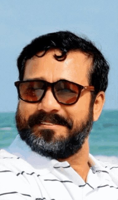 a man with a beard wears sunglasses and a white shirt