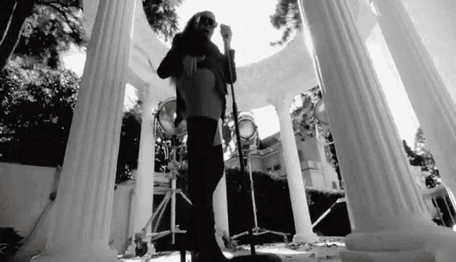 a man is singing into a microphone in front of columns