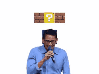 a man in a blue shirt is holding a microphone in front of a brick wall with a question mark on it .