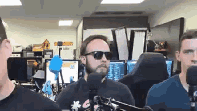 a man with a beard wearing sunglasses is standing in front of a microphone .