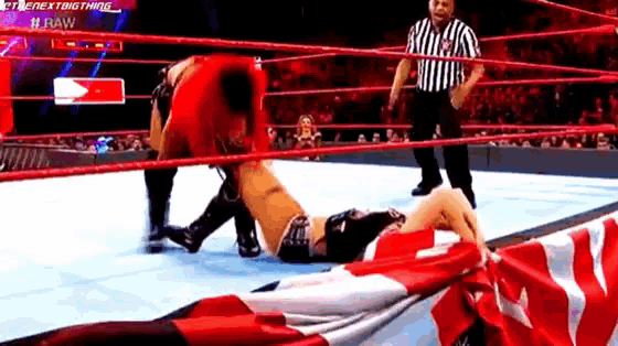 a wrestler is laying on the ground in a wrestling ring while a referee stands behind him .