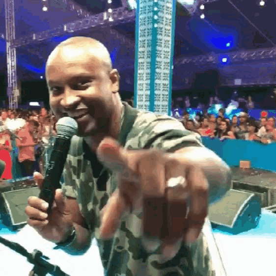 a man in a camouflage shirt is holding a microphone and pointing at the camera