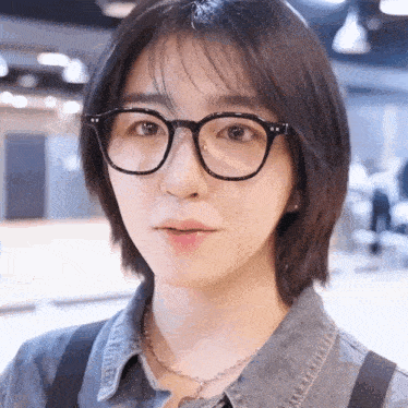 a woman wearing glasses and a blue shirt looks at the camera