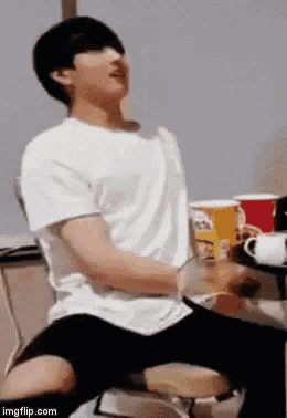 a man in a white shirt and black shorts is sitting on a chair with his legs crossed .