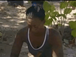 a woman in a blue tank top is sitting in the dirt on the beach .
