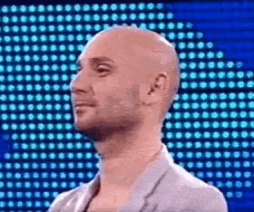 a bald man is smiling in front of a blue background