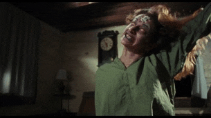 a woman in a green shirt is standing in a dark room with a clock in the background .