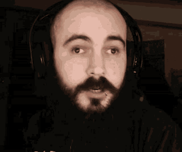 a man with a beard is wearing headphones and making a funny face .