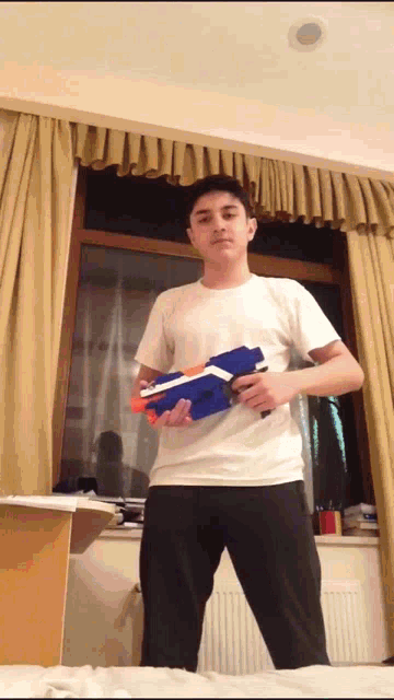 a young man in a white shirt holds a nerf gun