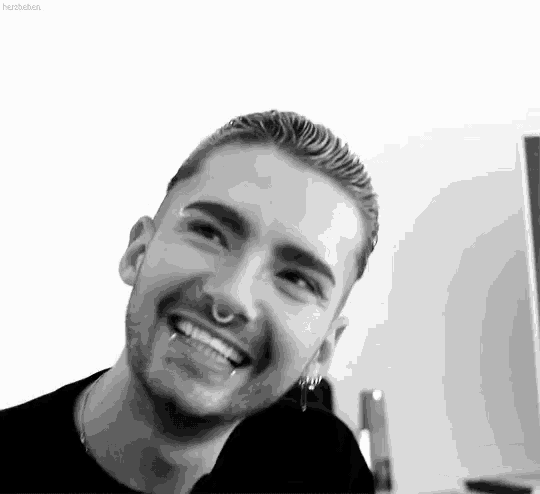 a black and white photo of a man with a nose ring and earrings smiling .