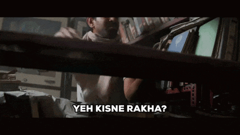 a man is sitting at a table in a library holding a tablet and a sign that says yeh kisne rakha .