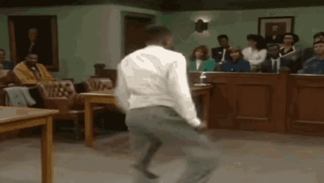 a man in a white shirt is dancing in front of a crowd in a courtroom
