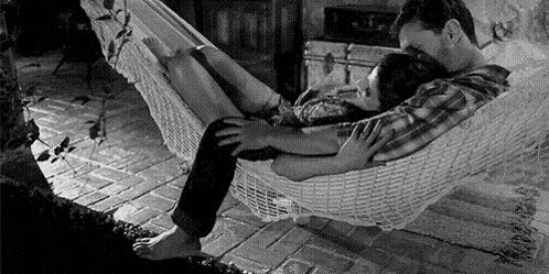 a man and woman are laying in a hammock .