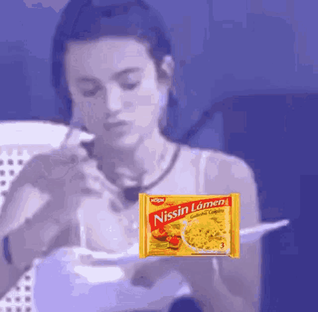 a woman is eating noodles with a package of nissin ramen in the foreground .