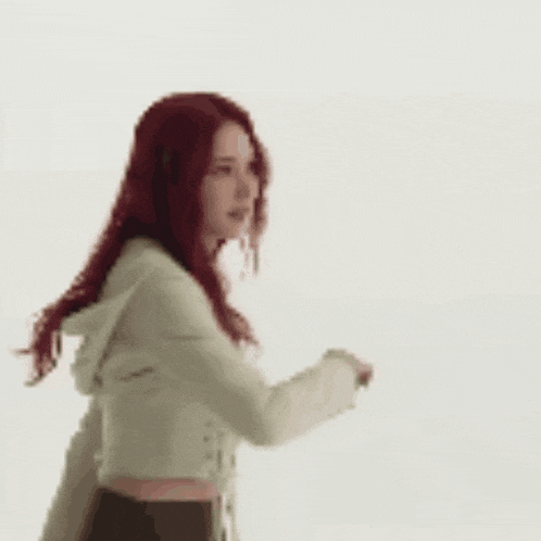 a woman with red hair is dancing in a white jacket and crop top .