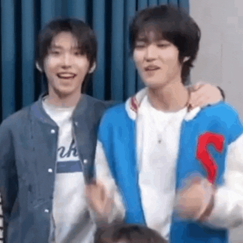 two young men are standing next to each other in front of a blue curtain and smiling .