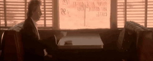 a man in a suit is sitting at a table in a diner looking out the window .