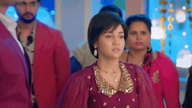 a woman in a purple dress is standing in front of a group of people in pink jackets .