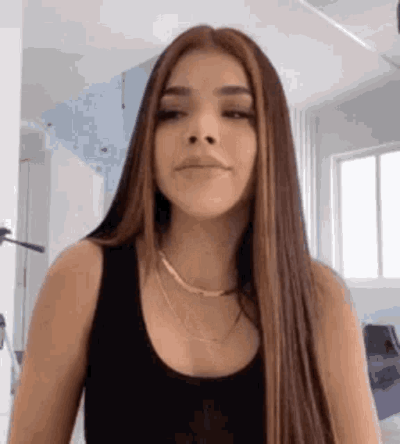 a woman with long hair is wearing a black tank top and a necklace .