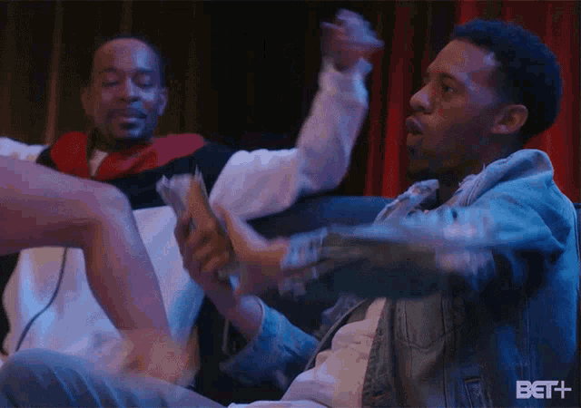 a man is holding a bunch of money while sitting on a couch with other men .