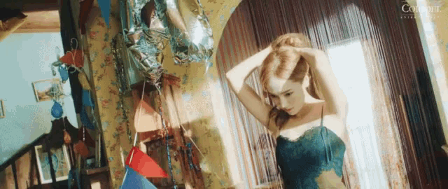 a woman in a blue dress is fixing her hair in a room with balloons and a mirror .