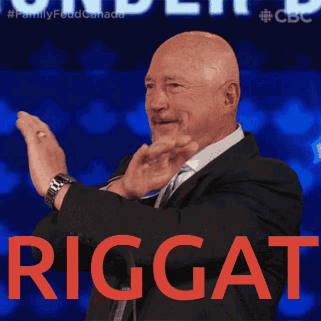 a man in a suit applauds in front of a blue background that says riggat