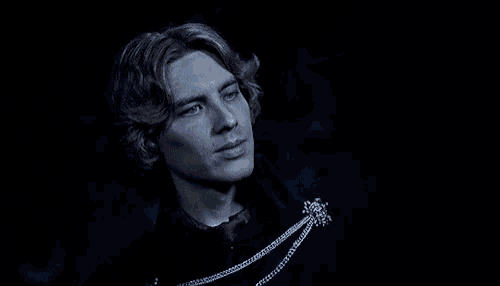 a man with blonde hair is wearing a black jacket and a necklace