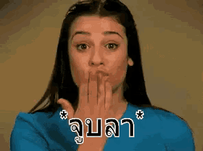 a woman in a blue shirt is blowing a kiss with a foreign language behind her